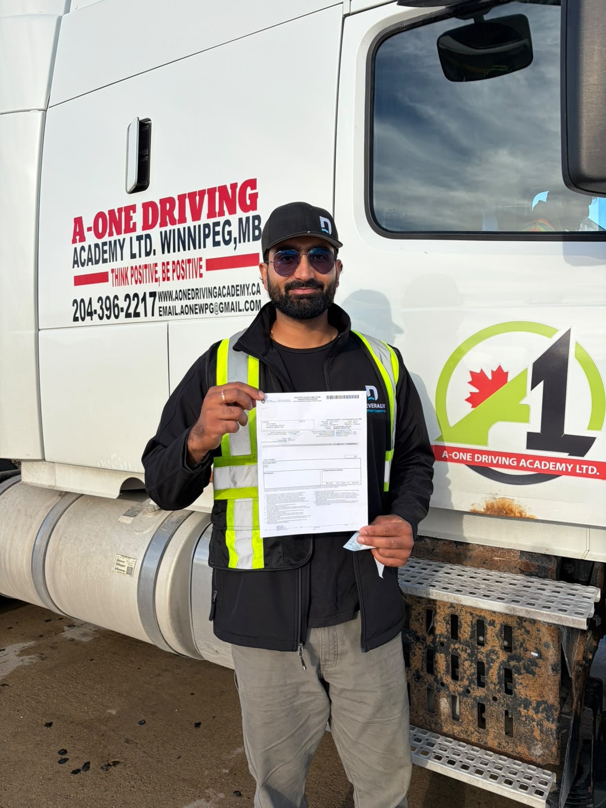 Graduate holding road test pass document beside A-One Driving Academy truck