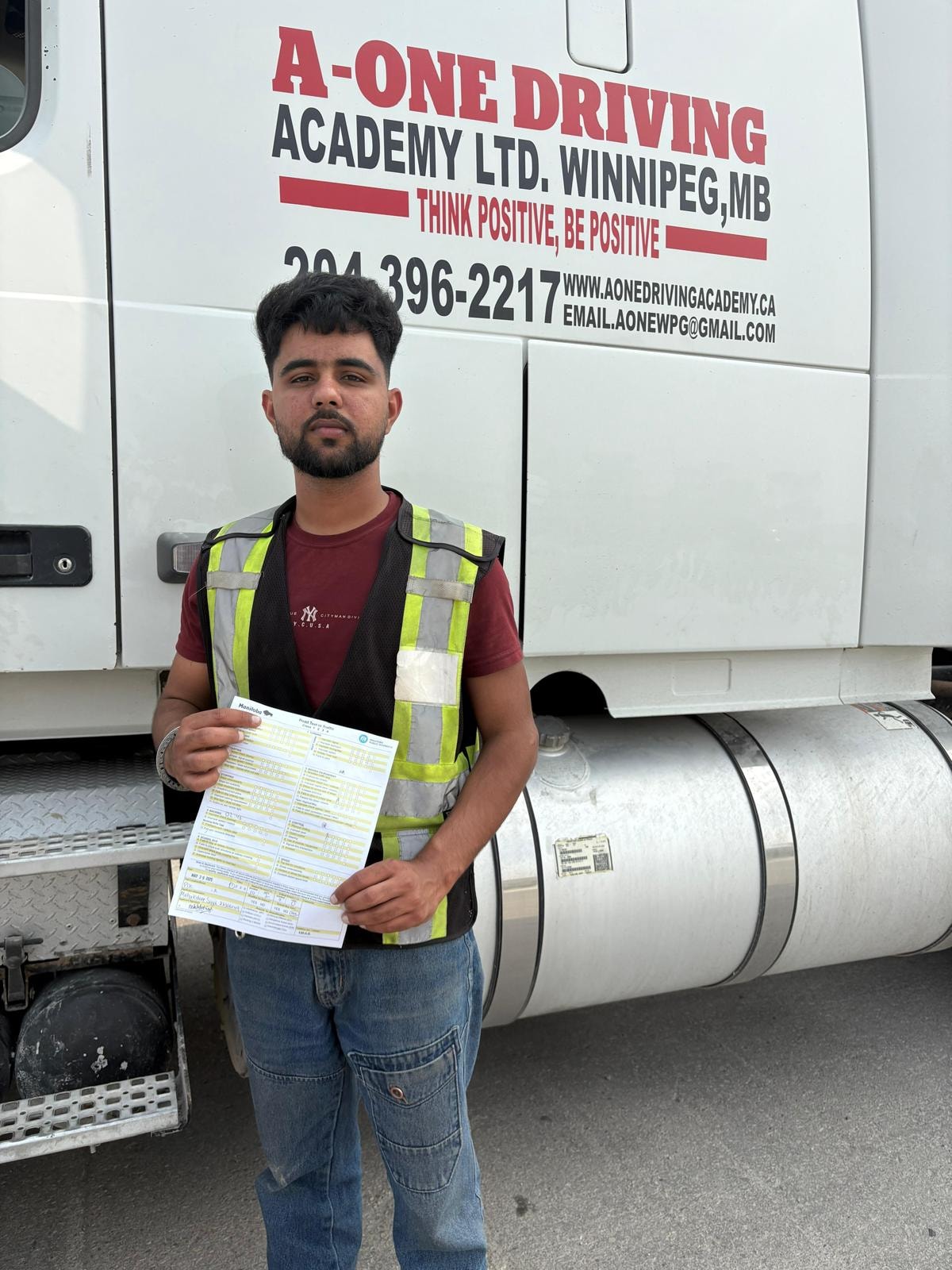 Student holding passed driving test document in front of A-One truck
