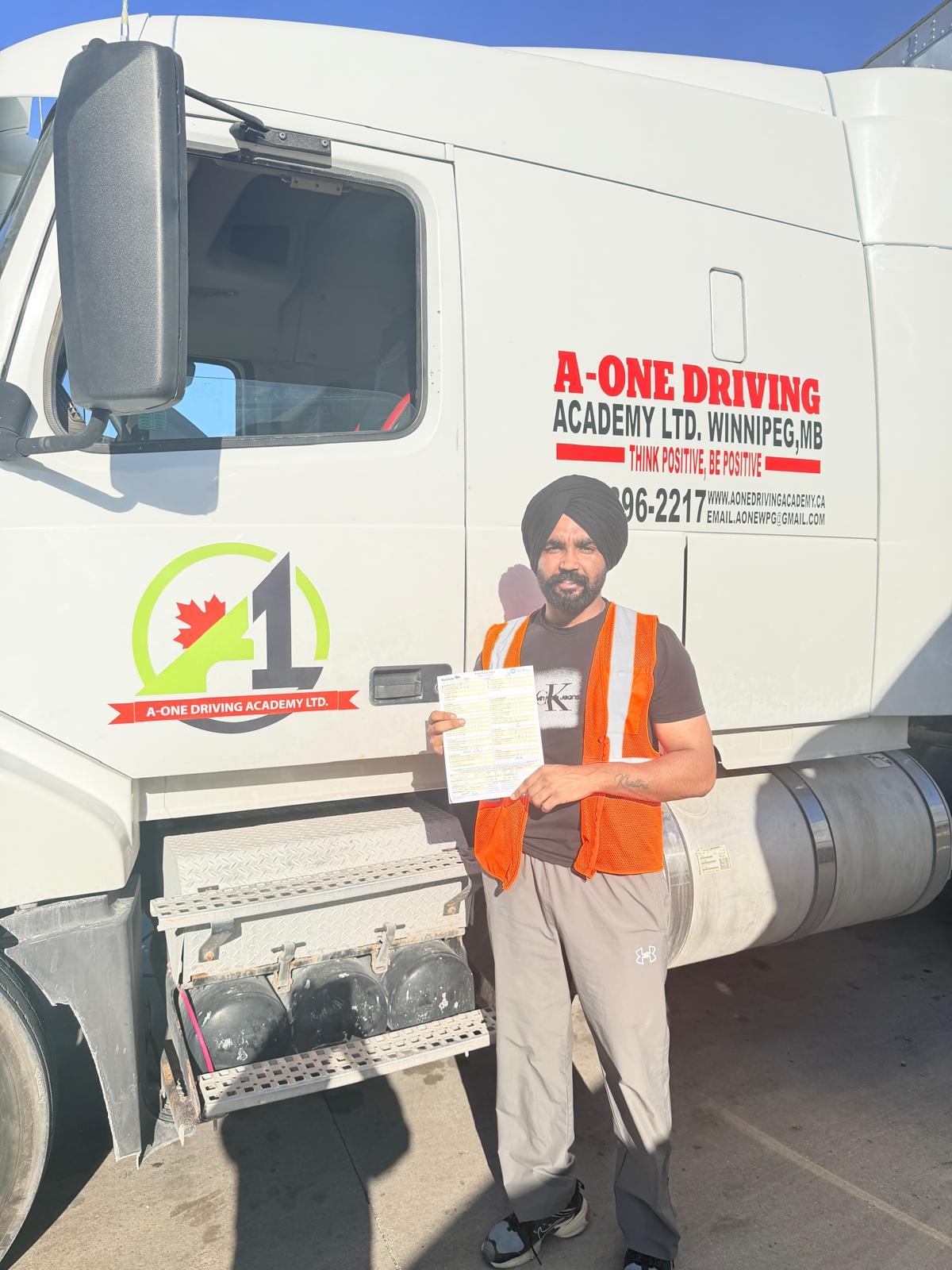 Student in orange safety vest holding road test pass document in front of A-One truck