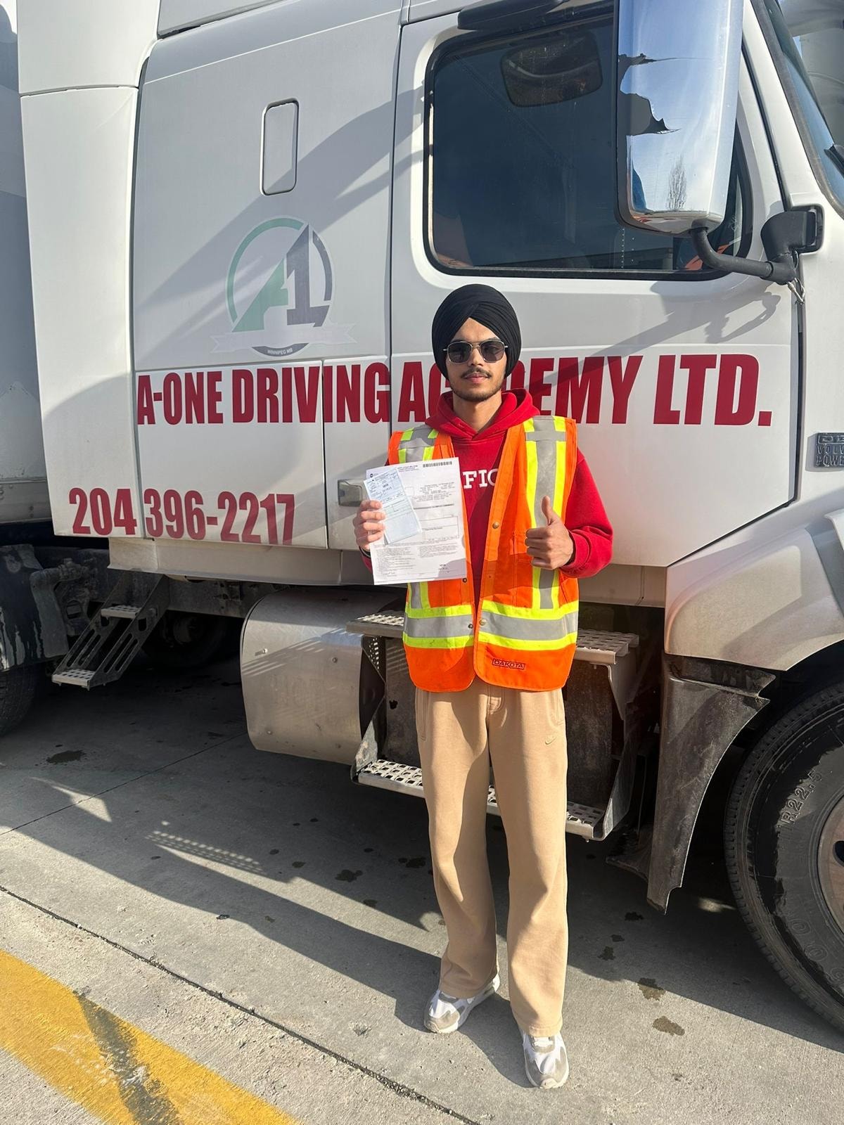 Young student in orange safety vest giving thumbs up with road test pass document