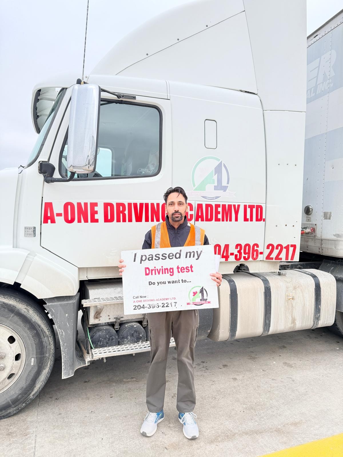 Graduate holding I passed my driving test sign in front of A-One Driving Academy truck